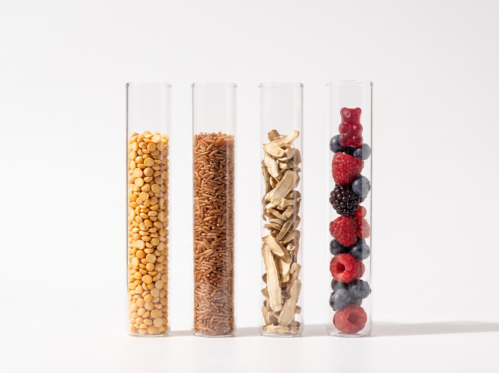 Four glass tubes holding split peas, brown rice, chicory root and berries with a gummy bear.